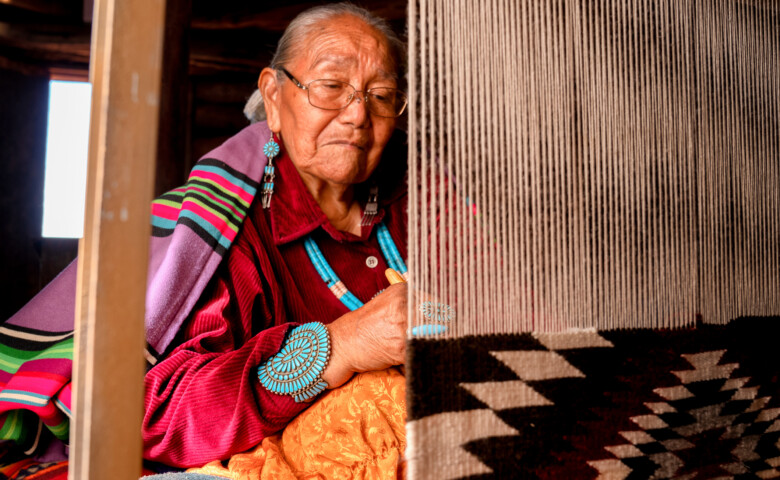 Traditional Navajo elderly woman working on a blanket loom in an authentic hogan