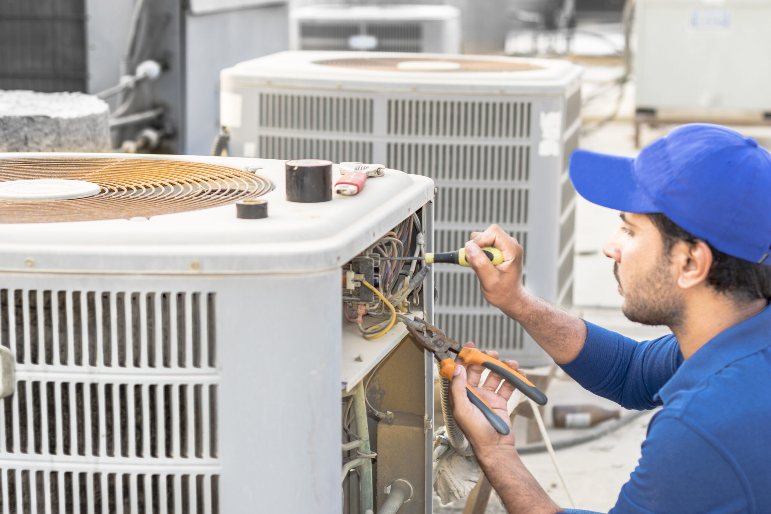 a professional electrician man is fixing the heavy unit of an air conditioner at the roof top of a building and wearing blue uniform and head cap a professional electrician man is fixing the heavy unit of an air conditioner at the roof top of a building and wearing blue uniform and head cap